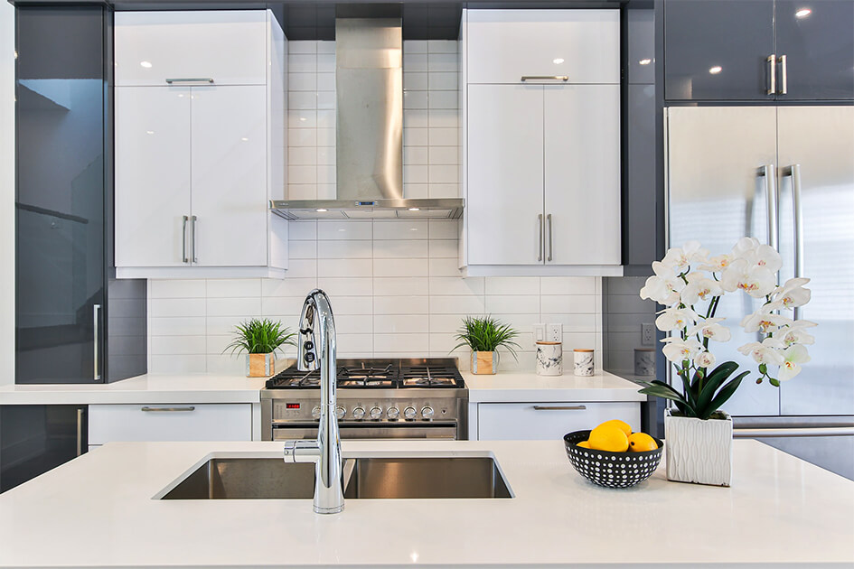 Een witte keuken met grijze elementen, een Amerikaanse ingebouwde koelkast en metalen dampkap